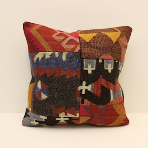May include: A colorful patchwork pillow with a geometric pattern in shades of red, blue, yellow, brown, and black.