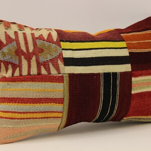 May include: A rectangular patchwork cushion with a variety of colourful stripes and patterns in shades of red, orange, yellow, brown, black, and white.