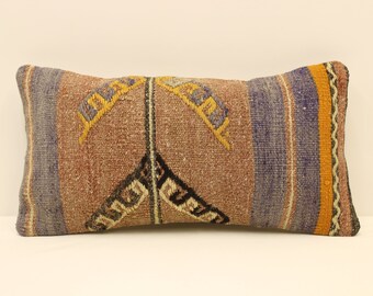 May include: A rectangular pillow with a woven pattern in shades of brown, blue, yellow, and black. The pillow has a geometric design with stripes and a central motif.