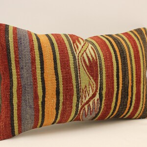 May include: A rectangular pillow with a striped pattern in shades of red, orange, yellow, green, and black. The pillow has a woven design with a stylized floral pattern.