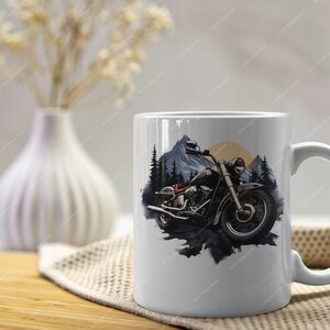 May include: White ceramic mug featuring a black and white illustration of a motorcycle in a mountain landscape. The motorcycle has a red seat and a black and white colour scheme.