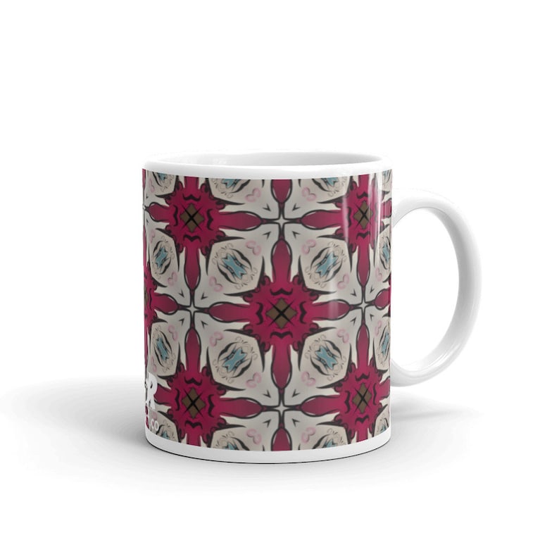 May include: White ceramic mug with a red, white, and blue geometric pattern. The pattern is a repeating design of stylized flowers.