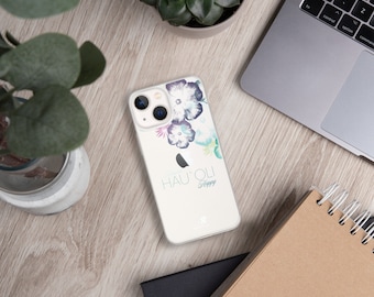 以下が含まれることがあります： 白いiPhoneケースに、花柄のデザインと「HAU'OLI Happy」という文字が印刷されています。
