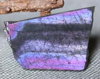 May include: A large, iridescent, black, purple, and blue gemstone with a rough, natural edge. The gemstone has a striated pattern and a smooth, polished surface.
