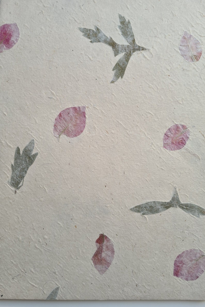 May include: A sheet of handmade paper with pressed pink flower petals and green leaves. The paper has a textured surface.