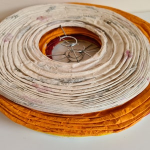 May include: A stack of paper lanterns in shades of orange, cream, and red. The cream-colored lantern has a floral pattern. The lanterns are circular and have a metal wire frame. The lanterns are stacked on top of each other.