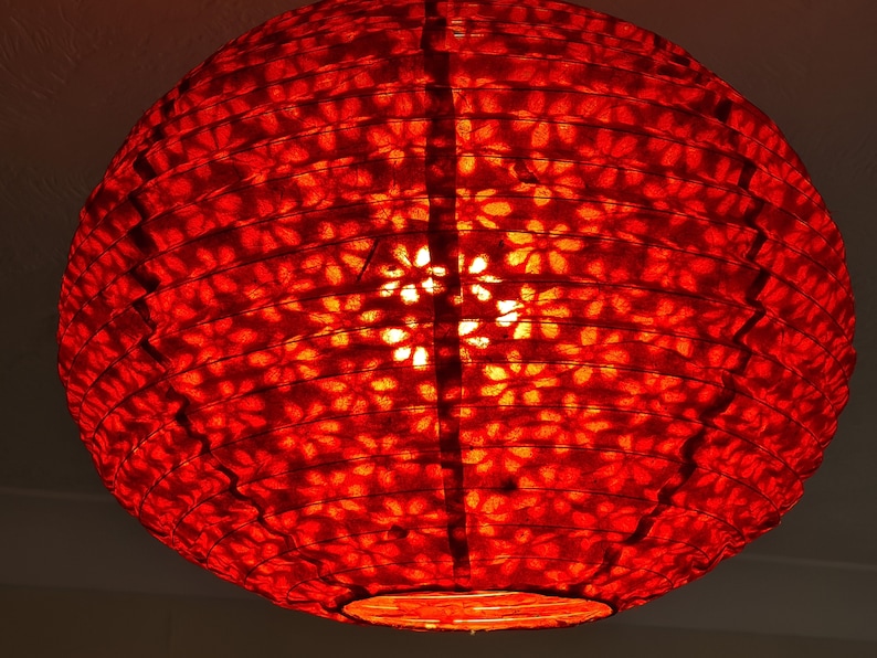 May include: A round, red paper lantern with a floral pattern. The lantern is lit from within, creating a warm, inviting glow. The design is visible through the translucent paper, adding a decorative element.