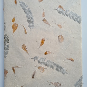 May include: A sheet of handmade paper with pressed leaves and petals. The paper is a light beige color and the leaves and petals are a light brown color.