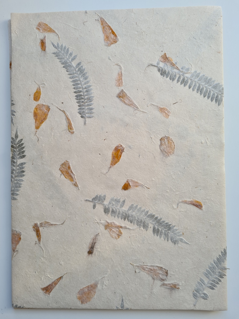 May include: A sheet of handmade paper with pressed leaves and petals. The paper is a light beige color and the leaves and petals are a light brown color.