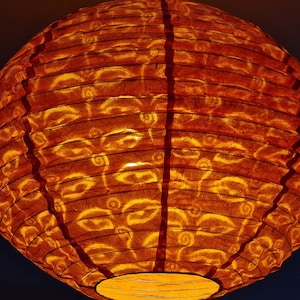 May include: A round, orange paper lantern with a warm glow. The lantern's surface has a textured appearance with a repeating pattern. The lantern is lit from within, creating a soft, inviting ambiance. Ideal for home decor.