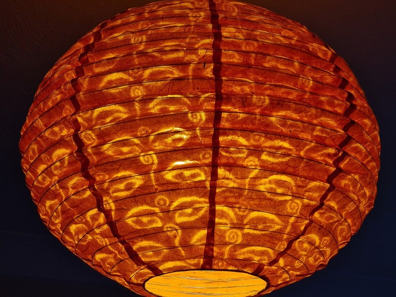 May include: A round, orange paper lantern with a warm glow. The lantern's surface has a textured appearance with a repeating pattern. The lantern is lit from within, creating a soft, inviting ambiance. Ideal for home decor.