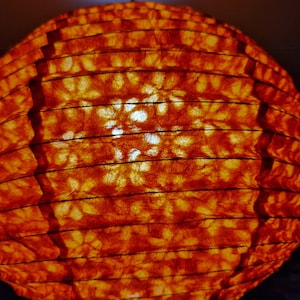 May include: A spherical, orange paper lantern with a ribbed design. The lantern's surface has a textured appearance, with visible patterns and a warm, inviting glow. The light source is visible through the paper, creating a soft, ambient light.