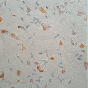 May include: A sheet of handmade paper with embedded dried flowers and leaves. The paper is a light beige color and the flowers and leaves are a light orange and gray.
