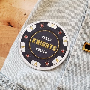 May include: A white and black embroidered patch with the text "Vegas Knights Golden" on a light blue denim jacket.
