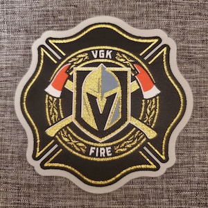 May include: A black and gold embroidered patch with a firefighter's cross design. The center features a gold knight's helmet with a black V and the text "VGK FIRE".