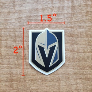 May include: A 2 inch by 1.5 inch vinyl sticker featuring the Vegas Golden Knights logo. The logo is a gold and black shield with a knight's helmet and a "V" inside.