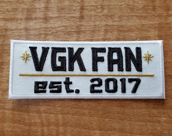 Peut inclure: Écusson brodé blanc avec du texte noir qui dit "VGK FAN" avec une ligne dorée et le texte "Est. 2017" en dessous.