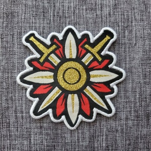 May include: A white and red embroidered patch featuring a gold sunburst design with two crossed swords. The patch has a black outline and a white border.