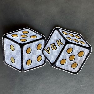 May include: Two white dice with black outlines and gold dots. One die has the letters "VGK" on it.