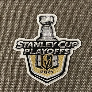 May include: A white and gold embroidered patch featuring the Stanley Cup Playoffs logo. The logo depicts a silver Stanley Cup trophy, the words "Stanley Cup Playoffs", and the Vegas Golden Knights logo with the year "2021" underneath.
