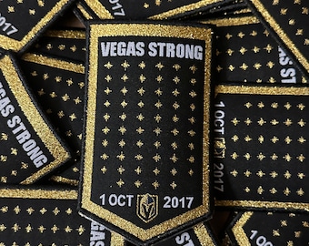 Peut inclure: Gros plan sur plusieurs patchs noirs et dorés avec le texte "VEGAS STRONG" et "1 OCT 2017". Les patchs sont en tissu et ont une finition pailletée.