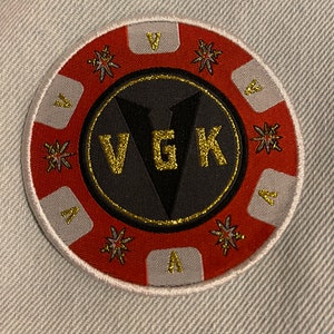 May include: Circular patch with a red and gray border, featuring the letters "VGK" in gold glitter on a black background. The patch has a gold trim and starburst designs, with the letter "A" in gray sections.