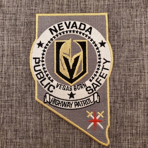 May include: Embroidered patch featuring the Nevada Public Safety Highway Patrol emblem. The patch is shaped like the state of Nevada, with a gray background and gold trim. The design includes text and a logo with black, gold, and white colors.
