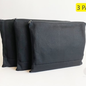 May include: Three black zippered pouches made of canvas fabric. The pouches are stacked on top of each other. The text "3 PACK" is printed in yellow on a white background.
