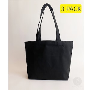 May include: A set of three black canvas tote bags with a 3 PACK label. The bags have long handles and are made of a durable material.