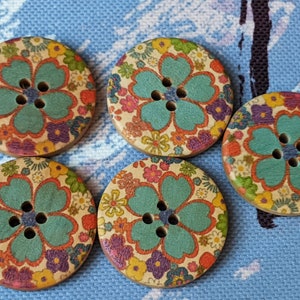 Könnte beinhalten: Fünf runde Holz-Knöpfe mit einem Blumenmuster. Die Knöpfe haben eine blaugrüne Blume mit weißem Rand und einen weißen Hintergrund mit einer Vielzahl von bunten Blumen.