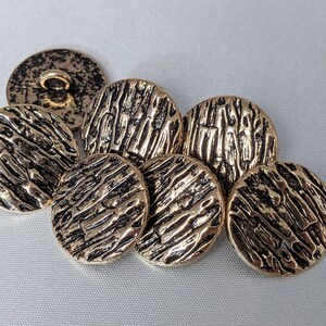 Könnte beinhalten: Sechs goldfarbene Knöpfe mit einem strukturierten Holzmaserungsmuster. Die Knöpfe sind rund und haben einen erhöhten Rand.