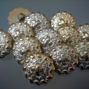 Könnte beinhalten: Eine Gruppe goldfarbener Knöpfe mit einem weißen Design. Die Knöpfe haben eine strukturierte Oberfläche und ein erhabenes Design.