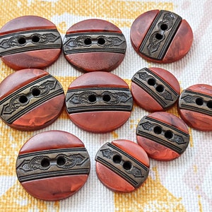 Könnte beinhalten: Eine Sammlung runder, rotbrauner Knöpfe mit einem dekorativen Metallband. Jeder Knopf hat zwei Löcher zum Annähen und ein detailliertes, verziertes Design auf dem Band. Die Knöpfe variieren leicht in Größe und Farbe.