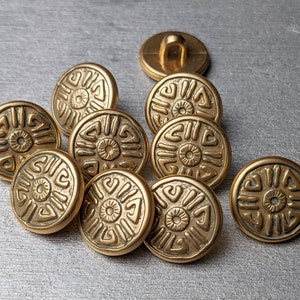 Könnte beinhalten: Zehn goldfarbene Knöpfe mit einem dekorativen, geometrischen Design. Die Knöpfe haben ein erhabenes, kreisförmiges Muster mit einem kleineren Kreis in der Mitte.