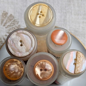 May include: Six vintage buttons in various colors and patterns, displayed in clear glass jars. The buttons are made of different materials, including pearl, plastic, and metal.