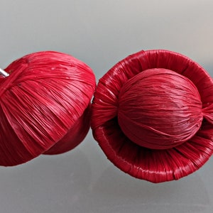 Può includere: Due ornamenti rotondi rossi intrecciati. Un ornamento ha un anello d'argento attaccato alla parte superiore. Entrambi gli ornamenti hanno una superficie intrecciata testurizzata.