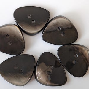 Op de afbeelding: Zes zwarte en grijze driehoekige knoppen met elk twee gaten.