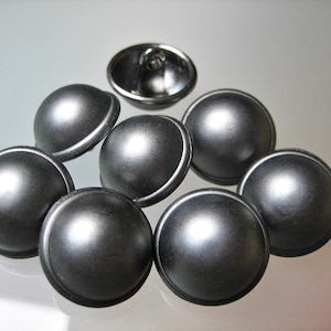 Könnte beinhalten: Acht silberfarbene Knöpfe mit einer erhabenen, abgerundeten Kuppelform und einer glatten, glänzenden Oberfläche.