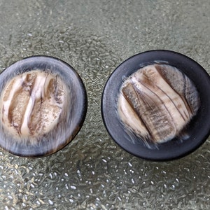 May include: Two round, black and white buttons with a marbled pattern. The buttons have a raised, white design.