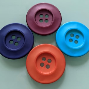 May include: Four large, round buttons in different colours: dark blue, burgundy, orange, and light blue. Each button has four holes in the centre.