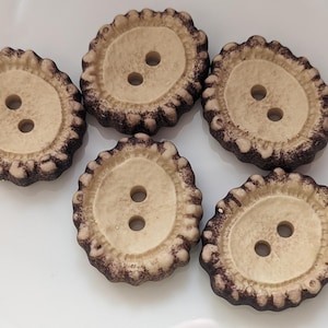 May include: Five decorative buttons with a light beige center and a dark brown, textured, antler-like border. Each button has two holes for sewing. The buttons are arranged on a white surface.