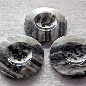 Op de afbeelding: Drie zwarte en witte swirl-patroon knoppen met elk vier gaten.