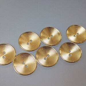 Könnte beinhalten: Sieben goldfarbene Knöpfe mit konzentrischem Kreisdesign. Die Knöpfe haben jeweils zwei Löcher.
