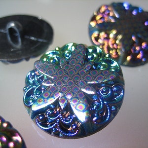 Può includere: Quattro bottoni iridescenti con un motivo floreale. I bottoni sono blu, verdi e viola con un riflesso metallico.