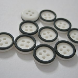 May include: A selection of white buttons, each with four holes and a dark grey rim. The buttons are displayed on a white surface. These buttons are suitable for sewing and craft projects, offering a classic design.