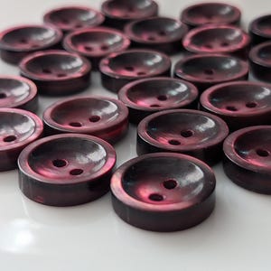 May include: A collection of 20 dark red, round, plastic buttons with two holes each. The buttons have a shiny, iridescent finish.