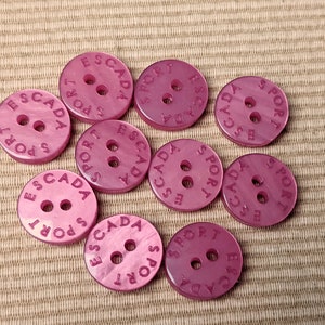 May include: Ten pink plastic buttons with the text "ESCADA SPORT" embossed on each button.