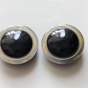 Op de afbeelding: Twee vintage ronde oorbellen. Elke oorbel heeft een grote, glanzende zwarte middensteen omgeven door een heldere, iriserende rand. De oorbellen staan tegen een witte achtergrond.