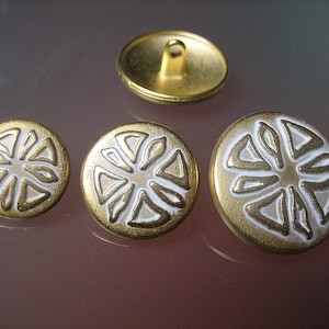 Op de afbeelding: Drie gouden knopen met een wit geometrisch ontwerp. De knopen hebben een reliëf en een gladde, glanzende afwerking.