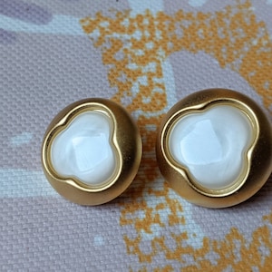 Könnte beinhalten: Ein Paar goldfarbene Ohrringe mit weißen, perlmuttartigen, kleeblattartigen Zentren.